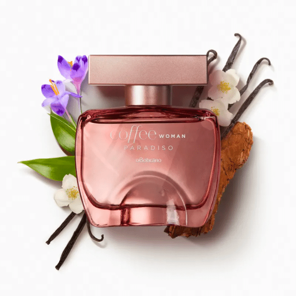 Frasco do Coffee Woman Paradiso na cor rosé gold e tampa na mesma cor. Atrás do frasco estão favas de baunilha e algumas flores que são compostos do perfume.