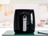 A foto mostra uma Air Fryer preta em um fundo de cozinha meio desfocado.