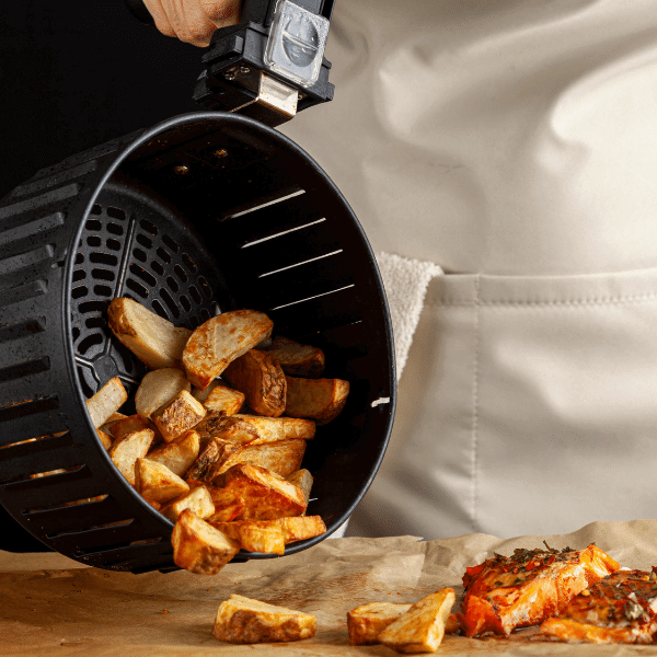 A foto mostra um chef de cozinha despejando uma cuba de air fryer cheia de batata frita.